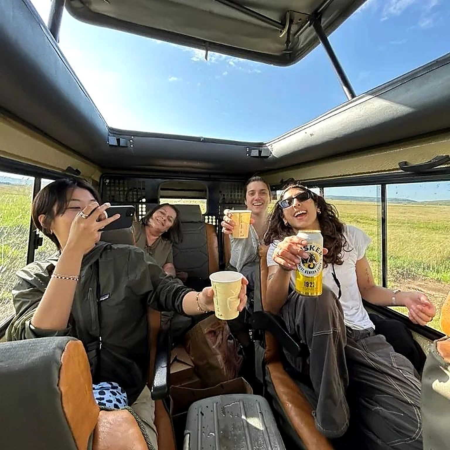A group of friends photographing a lion from their safari vehicle at sunset
